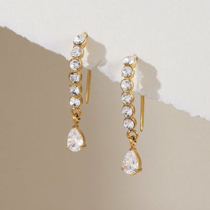 Solène crystal drop earrings hooked over a torn paper edge against a taupe background
