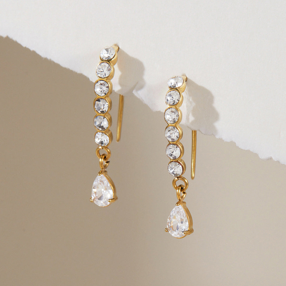 Solène crystal drop earrings hooked over a torn paper edge against a taupe background