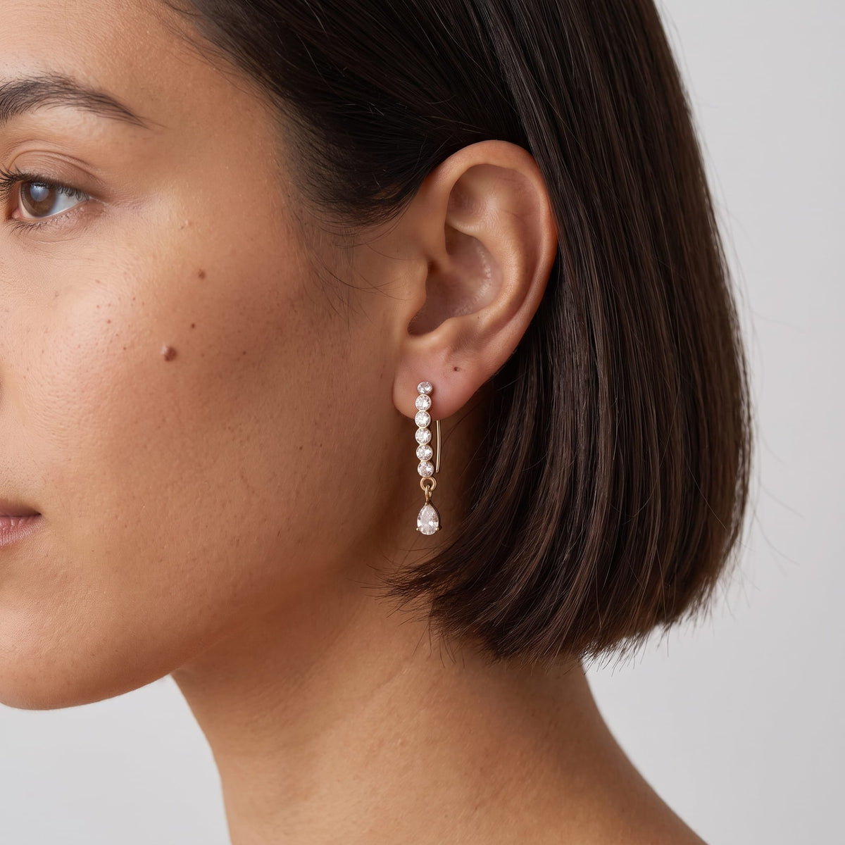 Woman wearing the Sol(ne crystal drop gold earrings on the ear, showing a profile view with dark short hair