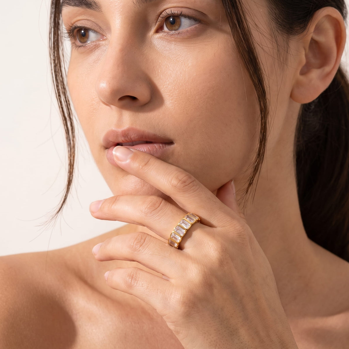 Woman wearing the Sophie baguette eternity gold ring on the hand posed near her chin