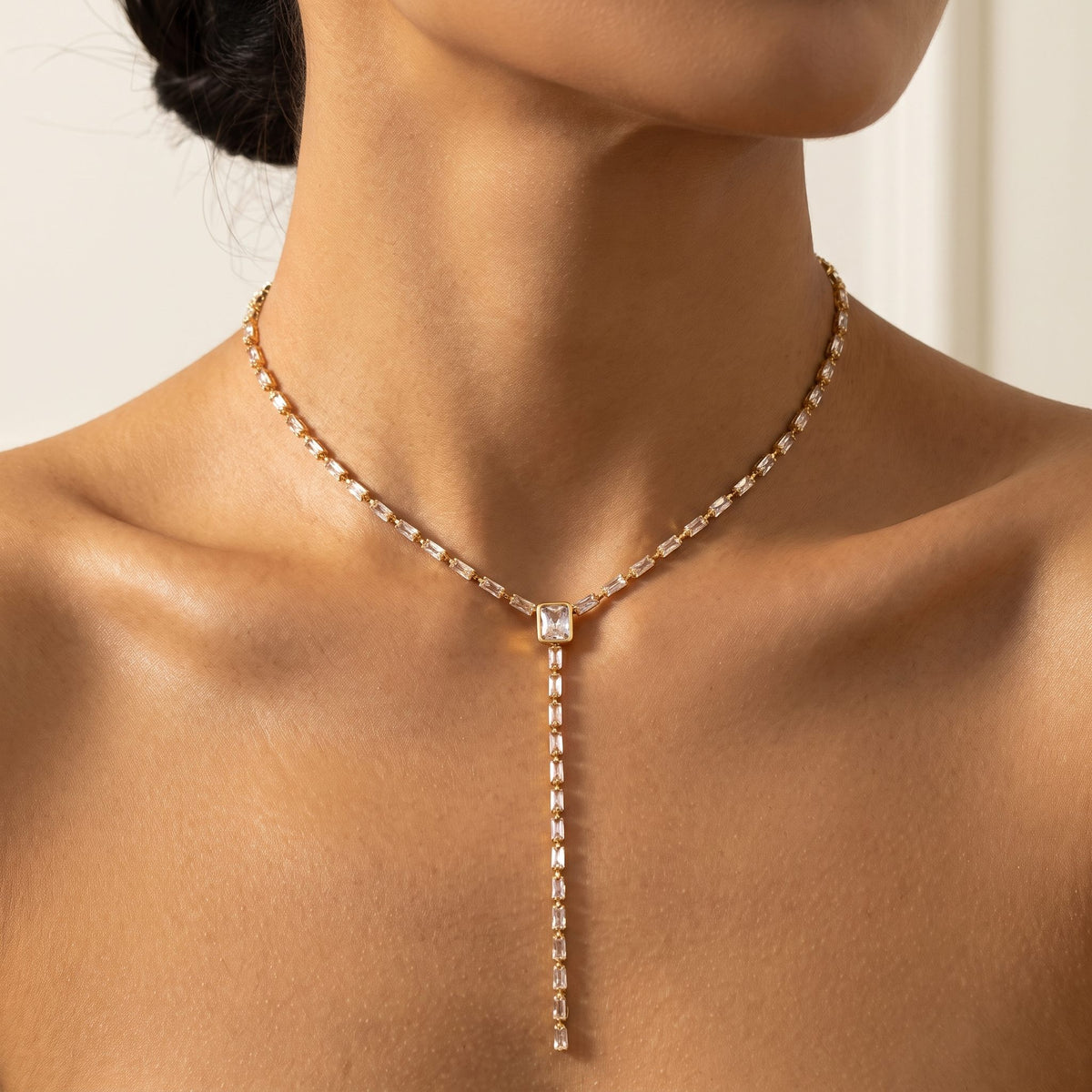 Close-up of a woman wearing the Sophie baguette lariat gold necklace at the base of her neck