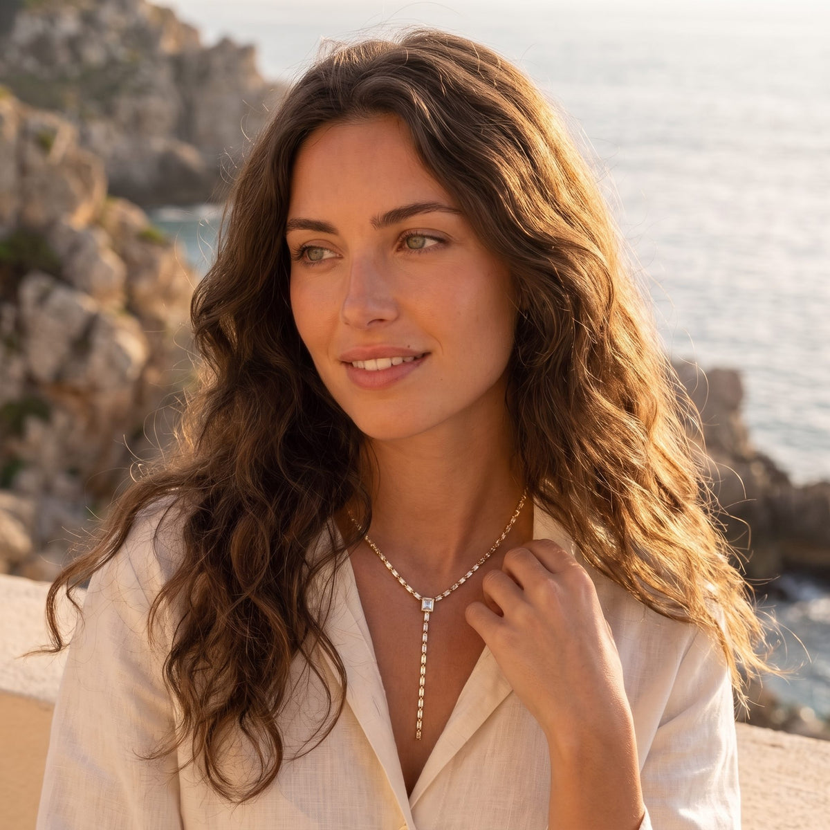 Woman by the sea at golden hour wearing the Sophie baguette lariat gold necklace