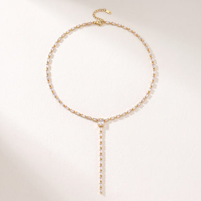 The Sophie baguette lariat gold necklace laid flat on an off-white surface