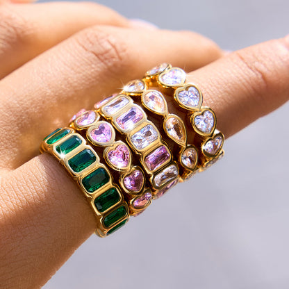 Hand wearing stacked eternity rings in green, pink and clear crystals, the green baguette band lowest