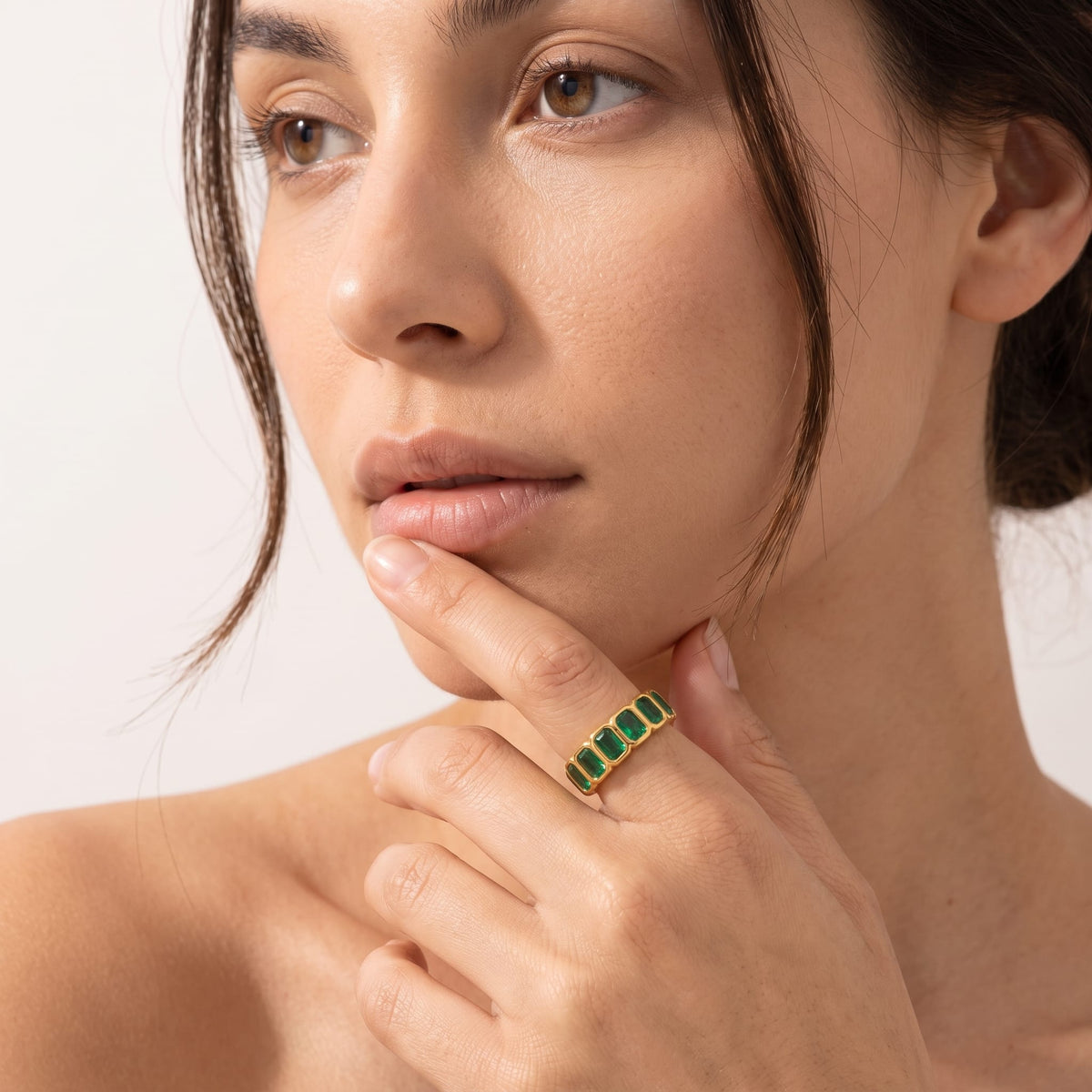 Woman wearing the Sophie green baguette gold ring on the hand resting near her chin