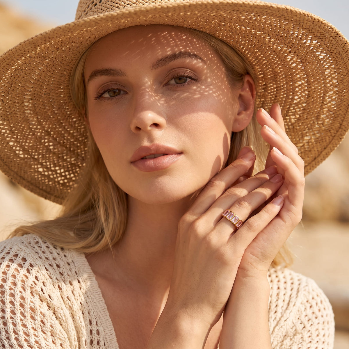 Woman wearing the Sophie pink baguette gold ring on the hand outdoors in a straw hat