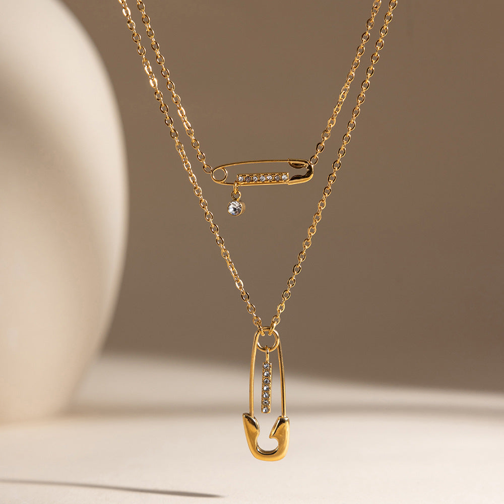 Stella safety pin gold necklace hanging in two layers against a soft beige backdrop