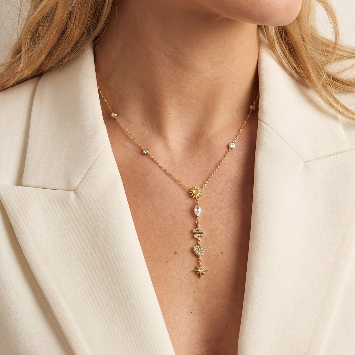 Woman wearing the Sybille talisman charm gold necklace at the collarbone, in a white blazer
