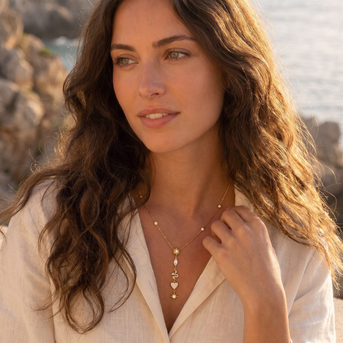 Woman wearing the Sybille talisman charm gold necklace at the collarbone in a loose beige shirt