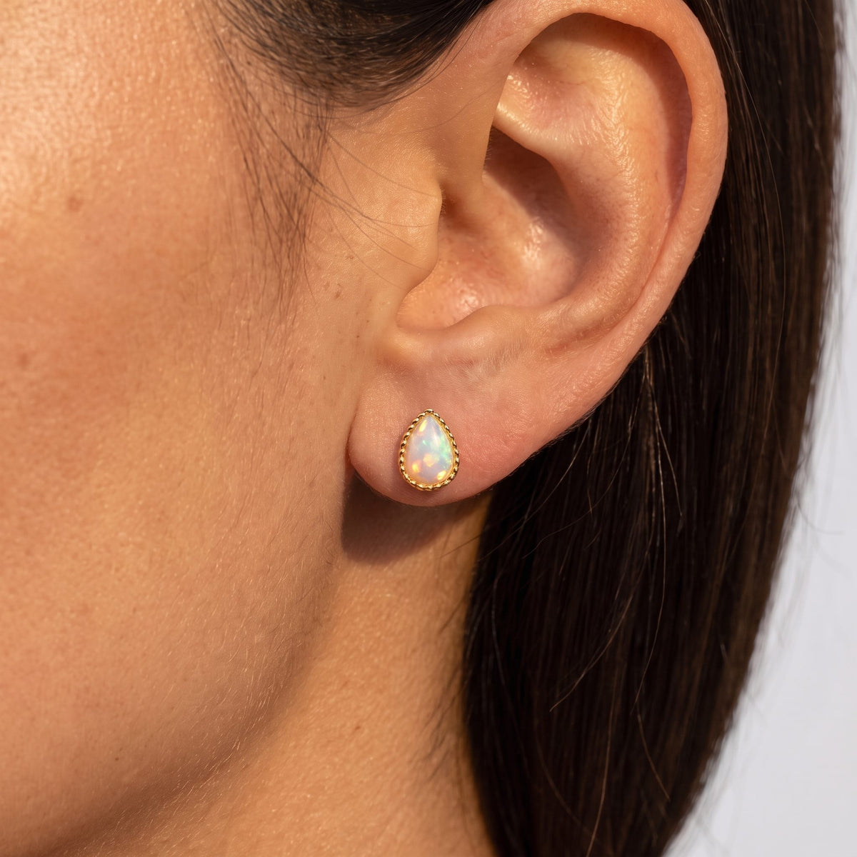 Woman wearing a Teadora opal teardrop stud in gold with a beaded rim on her lobe