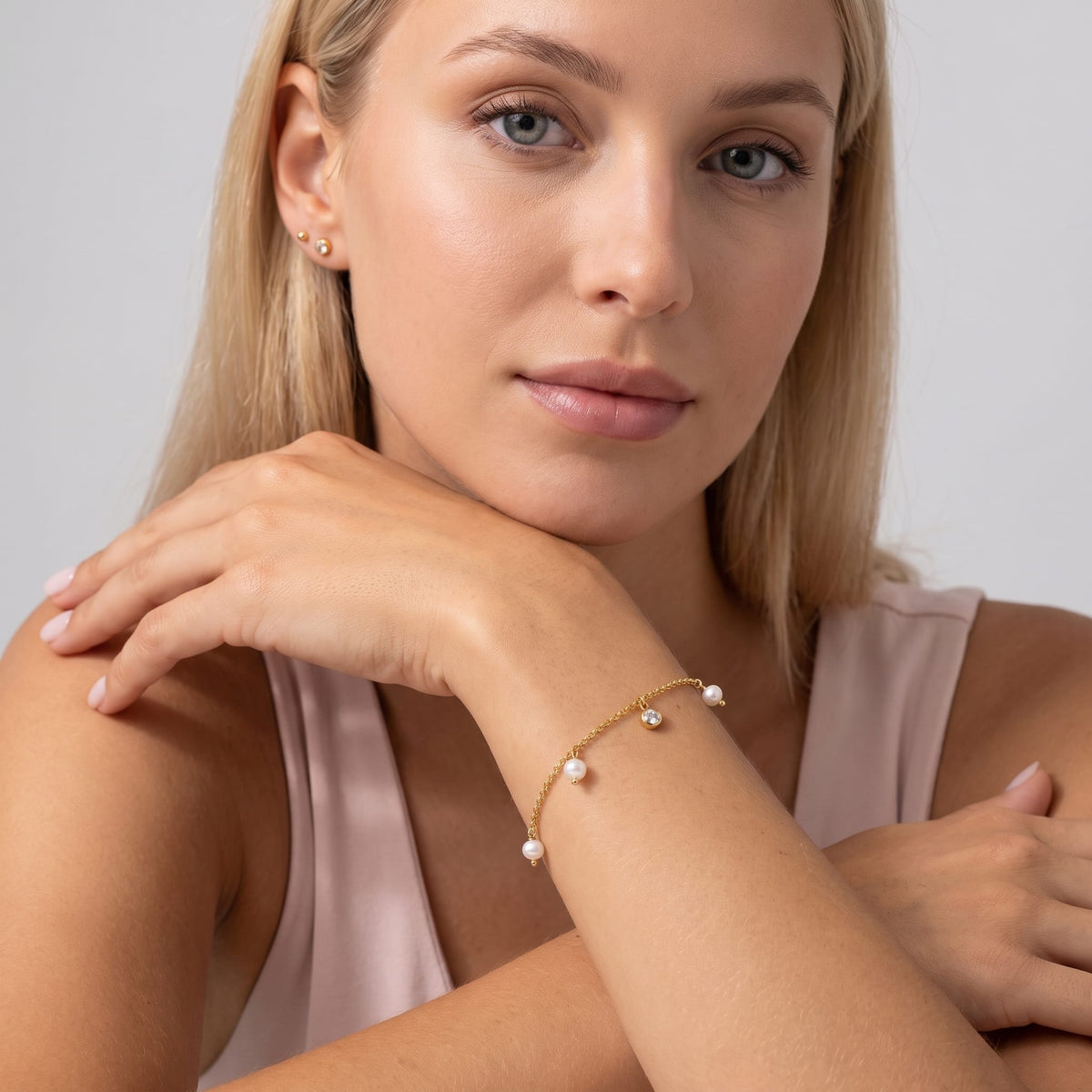 Woman wearing the Teresa pearl charm gold bracelet on the wrist resting her chin on her hand
