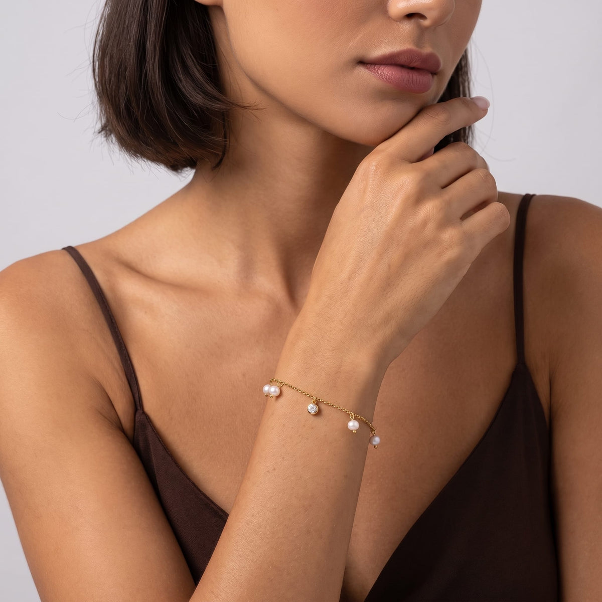 Woman wearing the Teresa pearl charm gold bracelet on the wrist while posing in a brown tank top