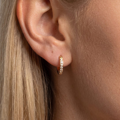Woman wearing the Tina gold huggie hoop lined with a row of tiny clear zircons