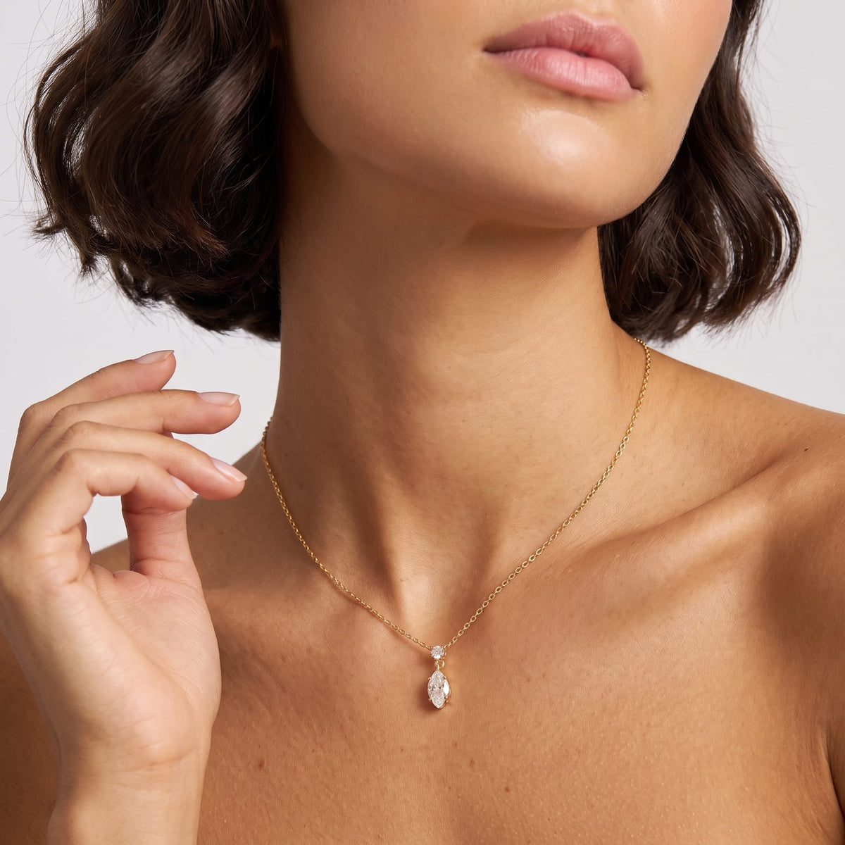 Woman wearing the Valentina marquise drop gold necklace at the throat with hand raised near neck