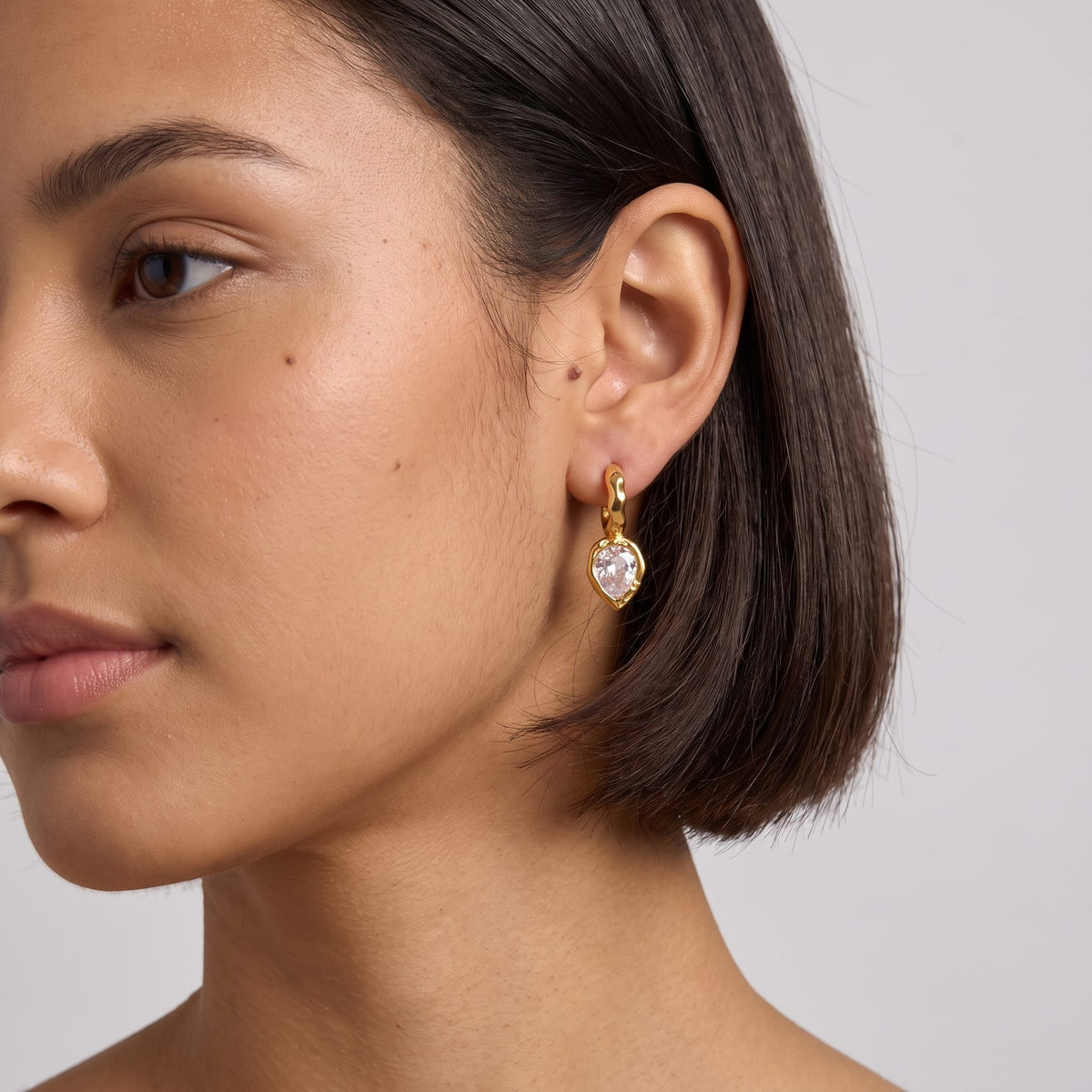 Woman wearing the Victoire hammered teardrop gold earrings on her ear with dark short hair