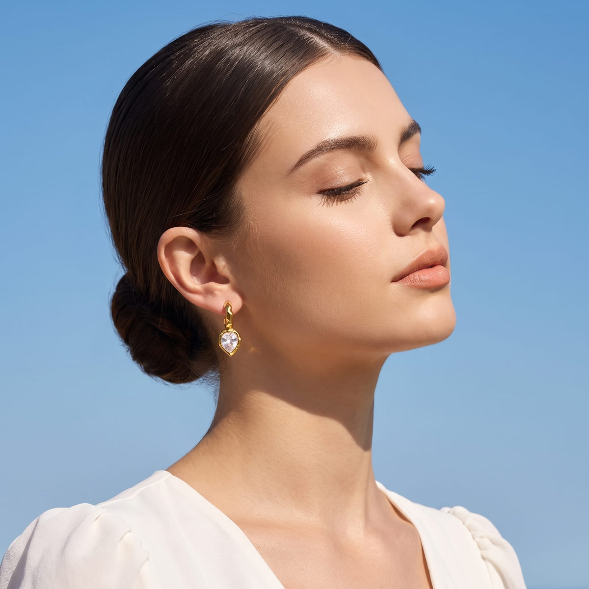 Woman wearing the Victoire hammered teardrop gold earrings on her ear against a blue sky