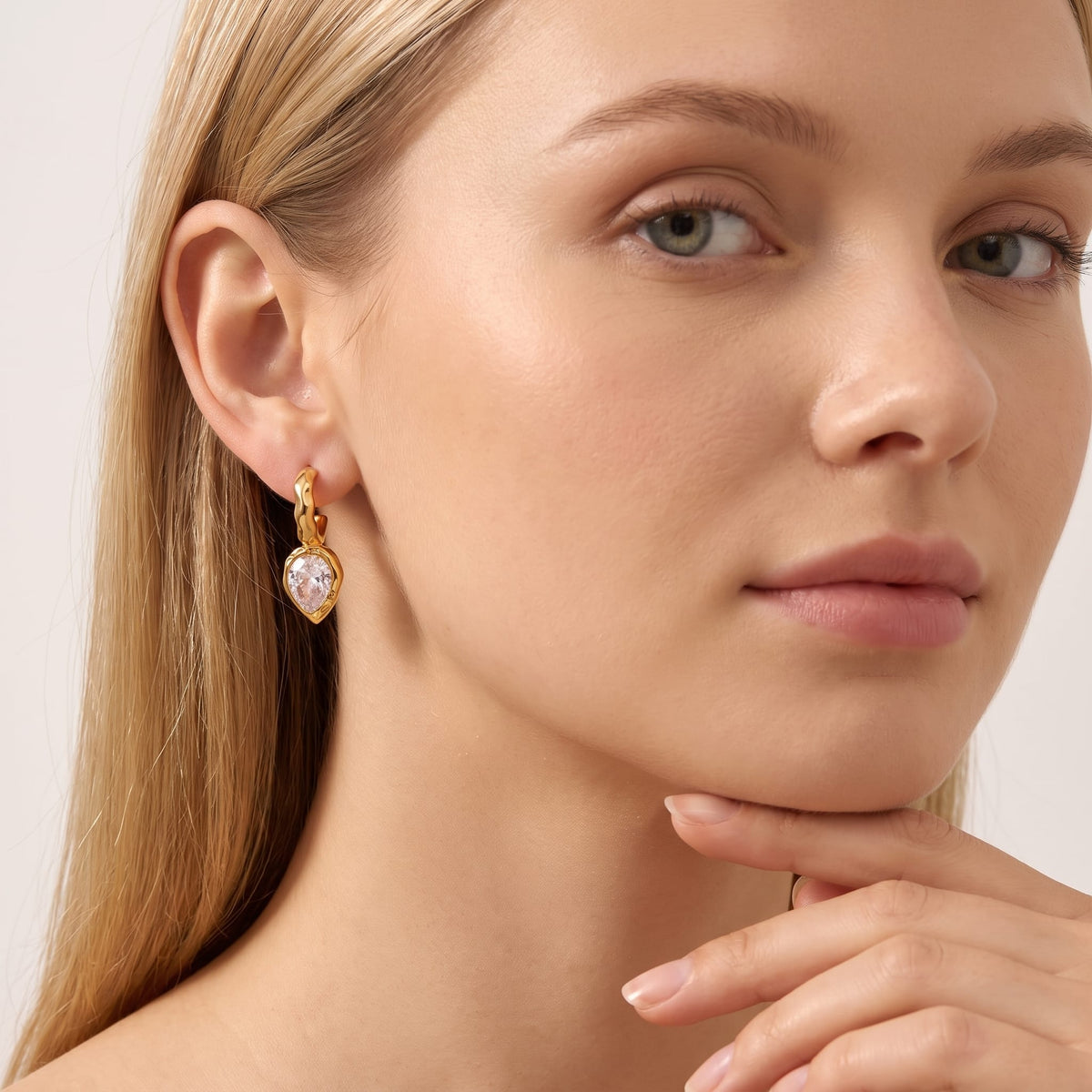 Woman wearing the Victoire hammered teardrop gold earrings on her ear with hand resting near chin