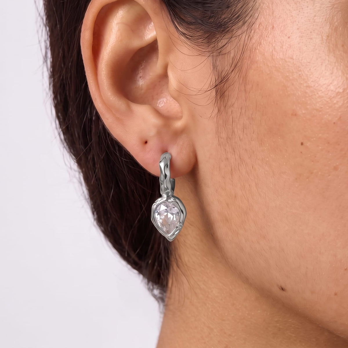 Woman wearing the Victoire hammered teardrop silver earrings on her ear in a close cropped view