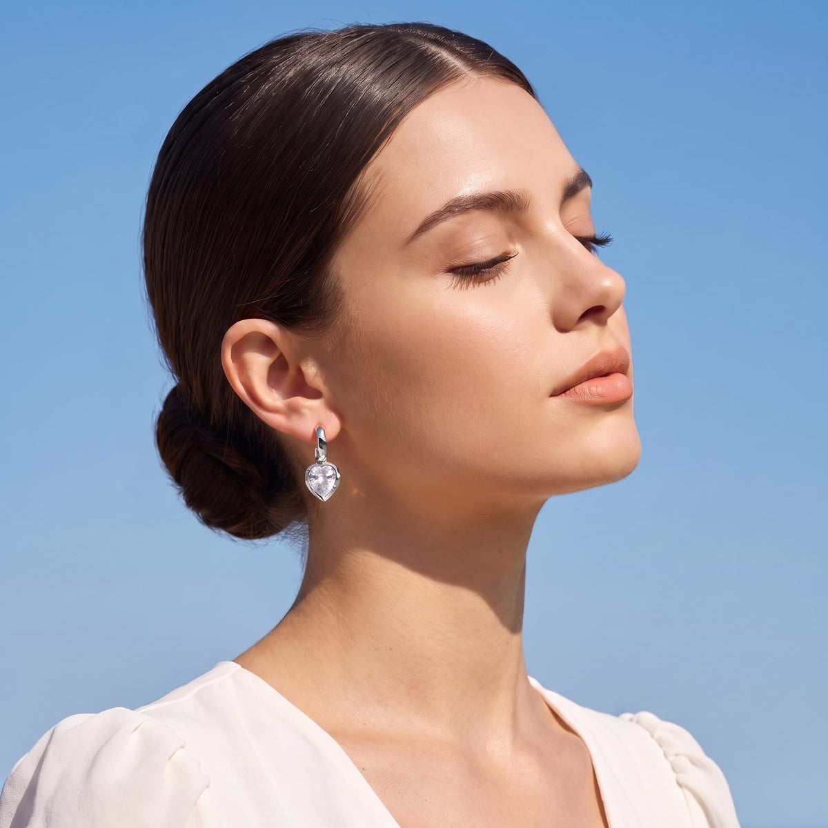 Woman wearing the Victoire hammered teardrop silver earrings on her ear against a blue sky
