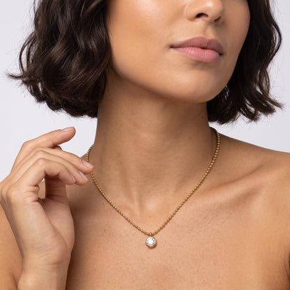 Woman with a dark bob wearing the Vida crystal bezel gold necklace, one hand raised near her neck