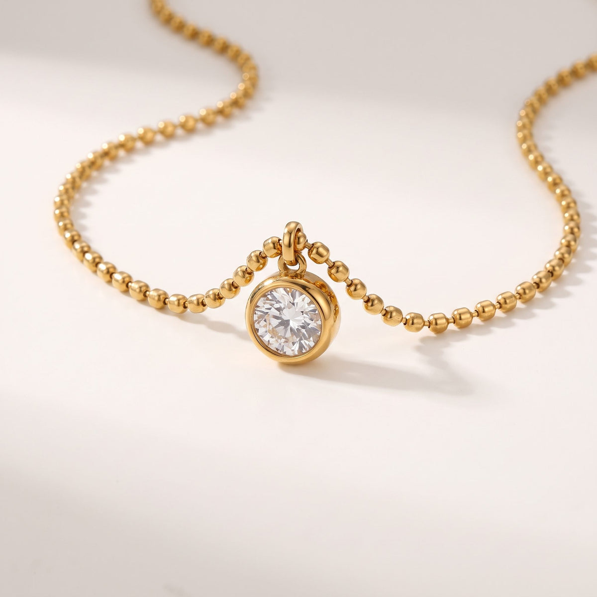 Close-up of the Vida crystal bezel gold necklace on an off-white surface