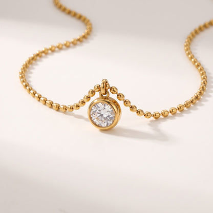 Close-up of the Vida crystal bezel gold necklace on an off-white surface