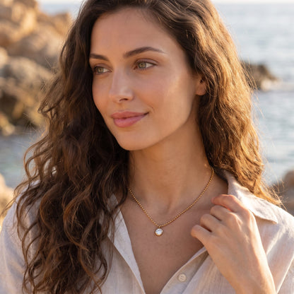 Woman by the sea at golden hour wearing the Vida crystal bezel gold necklace