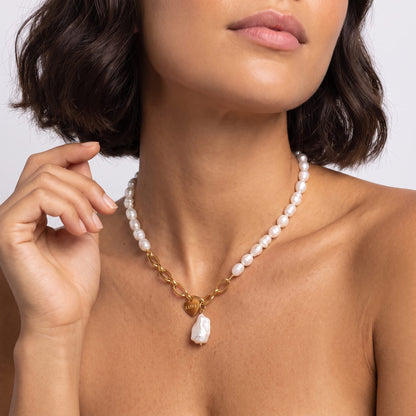 Woman wearing the Vivienne pearl love gold necklace at the collarbone with her hand raised