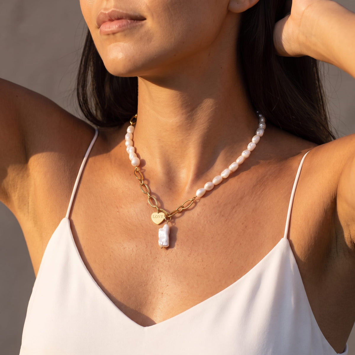 Woman wearing the Vivienne pearl love gold necklace at the collarbone in a white top