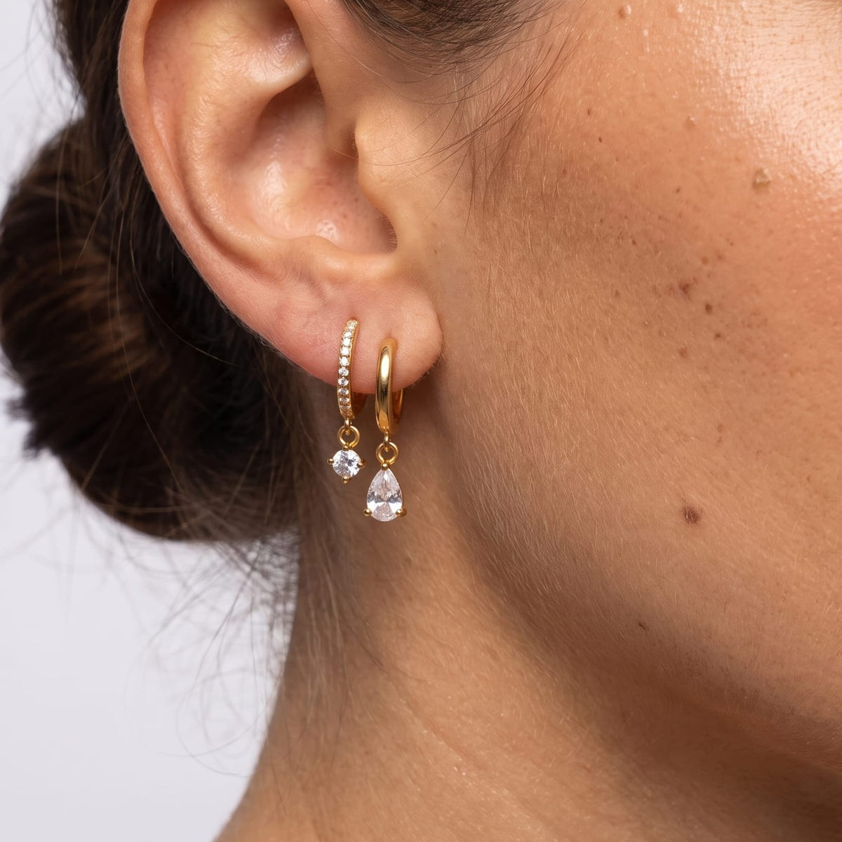 Woman wearing the Ysaline double hoop gold earrings on her earlobe in a close up studio shot