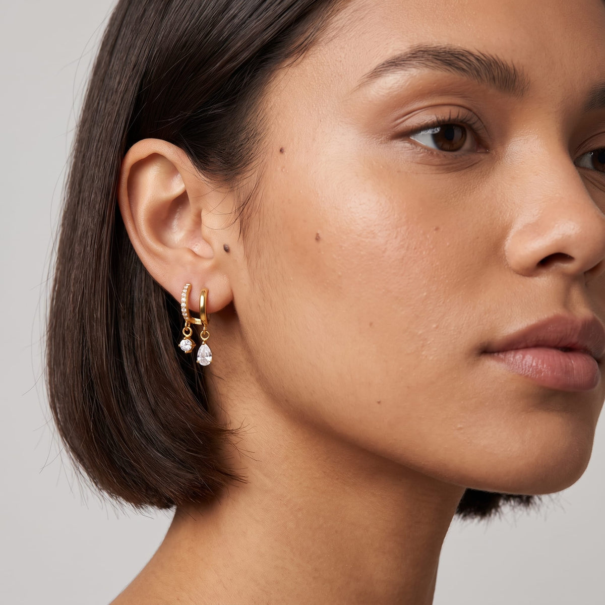 Woman wearing the Ysaline double hoop gold earrings on her earlobe with short dark hair
