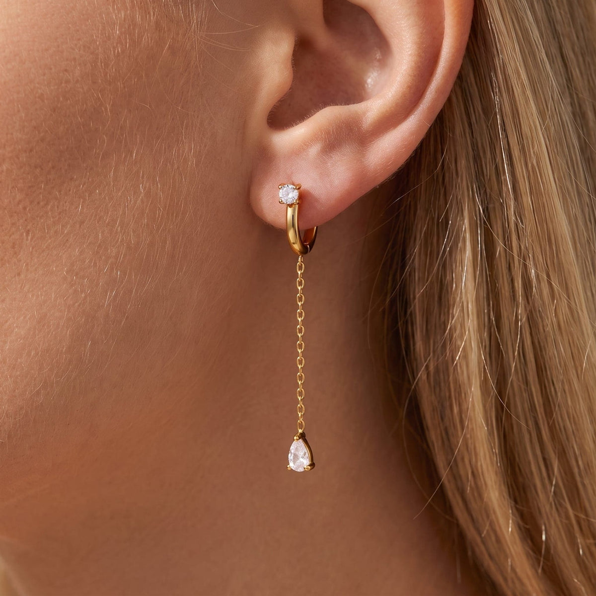 Woman wearing the Yvette chain drop gold earrings on the ear, with a teardrop crystal