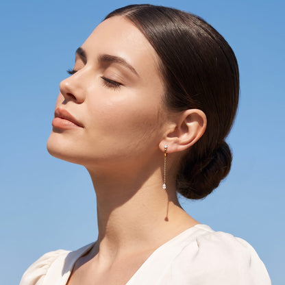 Woman wearing the Yvette chain drop gold earrings on the ear against a blue sky