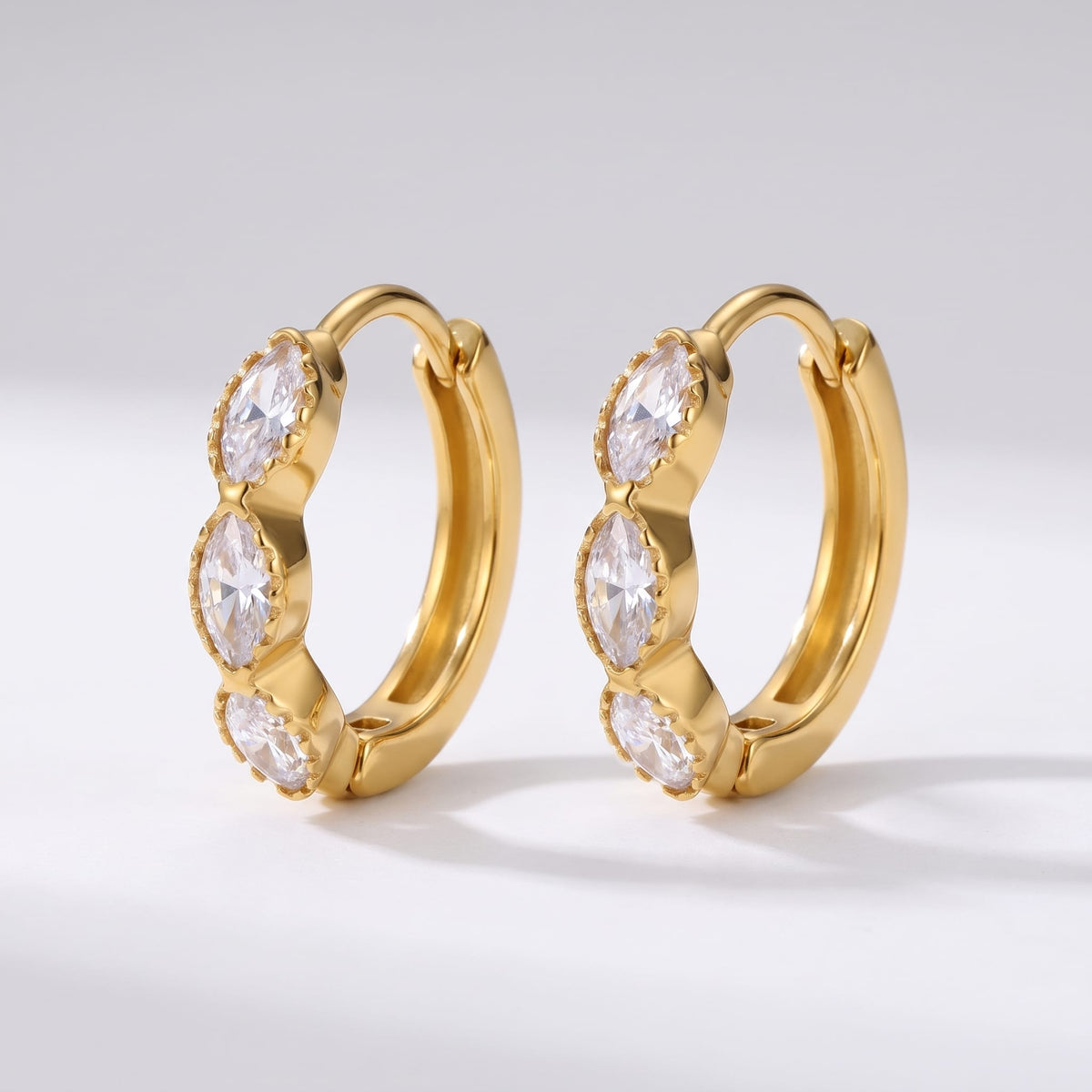 Zoé marquise huggie gold earrings on a light gray surface